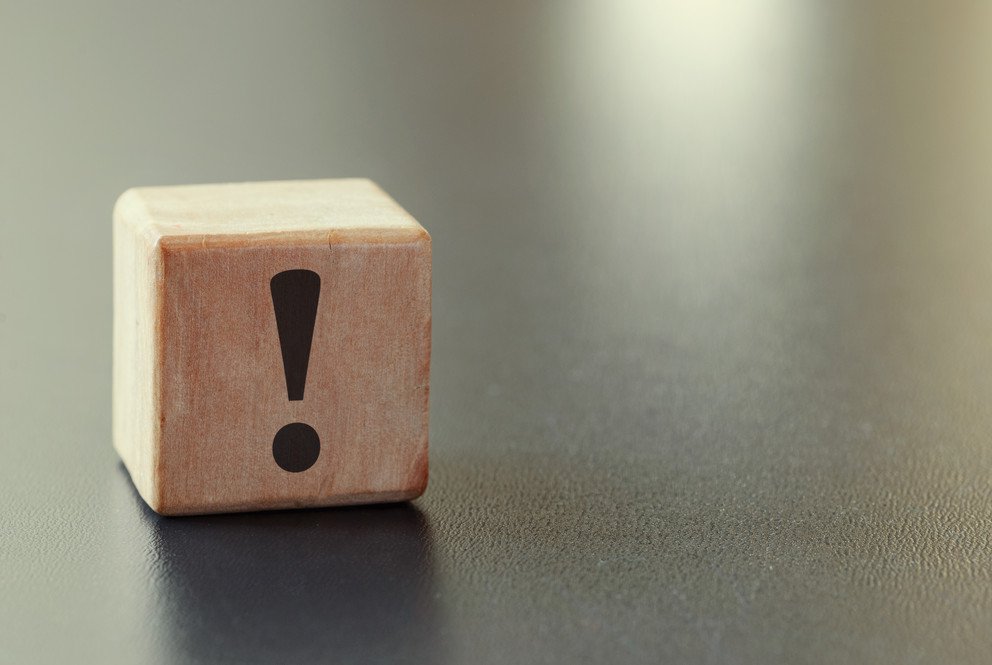 Symbolic image for important information, represented by a wooden cube with a black exclamation mark on it